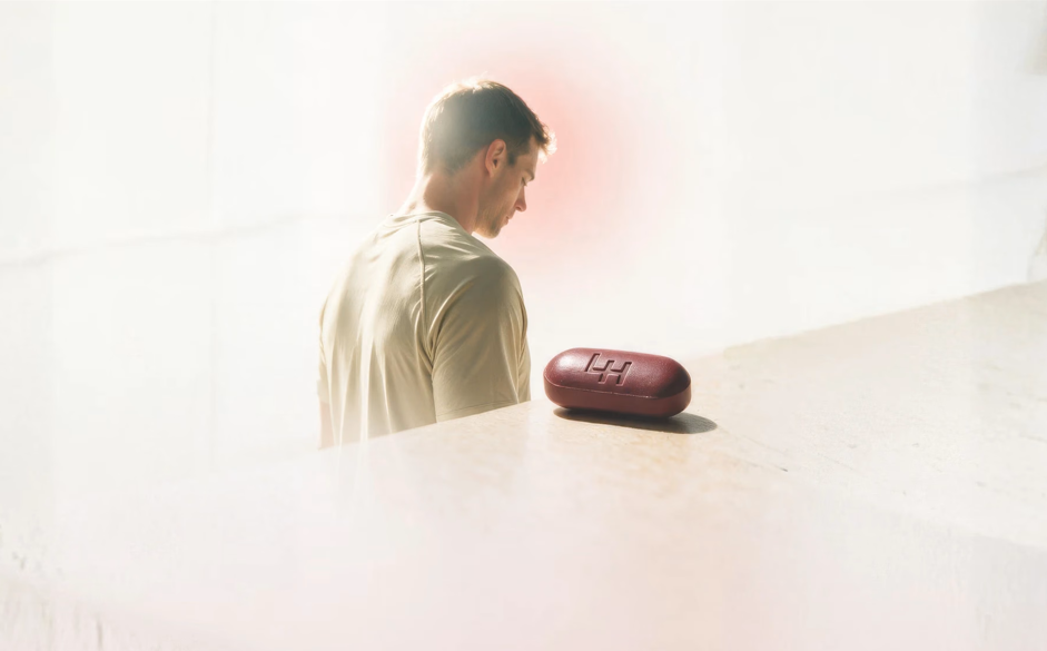 A man looking down at a red Leader Health case on a sunlit ledge.